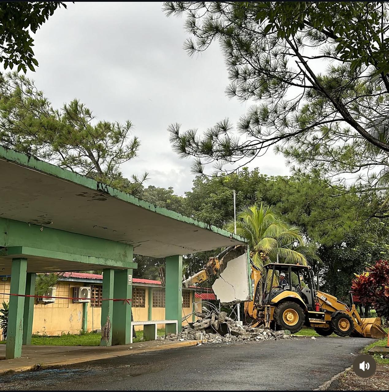 Excavadora con pinza demoledora derribando un edificio de concreto con riego para control de polvo